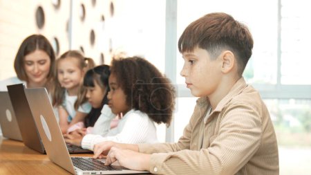Photo for Boy playing laptop with multicultural friend learning prompt at STEM technology class. Multicultural student study about engineering code and programing system with blurring background. Erudition. - Royalty Free Image