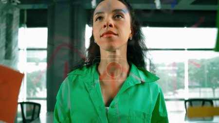Photo for Portrait of skilled young beautiful hispanic project manager thinking about marketing idea. Professional businesswoman making business plan by using sticky notes at glass board in office. Manipulator. - Royalty Free Image