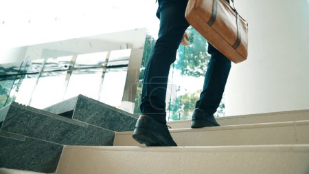 Téléchargez les photos : La jambe d'un homme d'affaires monte les escaliers. Un homme qui a réussi à monter les escaliers tout en explorant une nouvelle chose. Représenté voyager, obtenir une promotion, trouver un nouvel emploi, augmenter les compétences. Exultant. - en image libre de droit