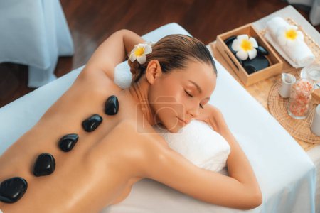 Photo for Hot stone massage at spa salon in luxury resort with day light serenity ambient, blissful woman customer enjoying spa basalt stone massage glide over body with soothing warmth. Quiescent - Royalty Free Image