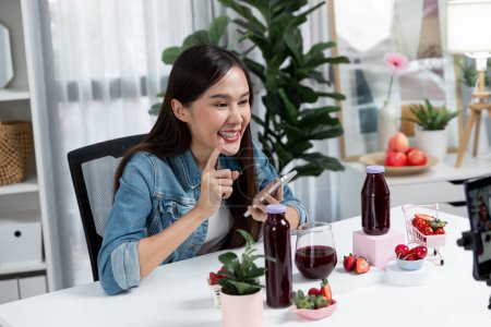 Photo for Smiling young beautiful Asian reviewing tasty mixed strawberry and cherry juice detox drinks, showing healthy product to promote for special promotion selling on social media online record. Stratagem. - Royalty Free Image