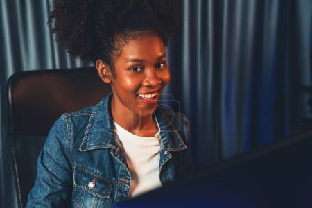 Téléchargez les photos : Jeune femme afro-américaine au visage surprise, portant une chemise en jeans bleu et regardant le document final du projet sur un ordinateur portable pour planifier la prochaine séquence. Concept de travail à la maison soignée. Tastemaker. - en image libre de droit