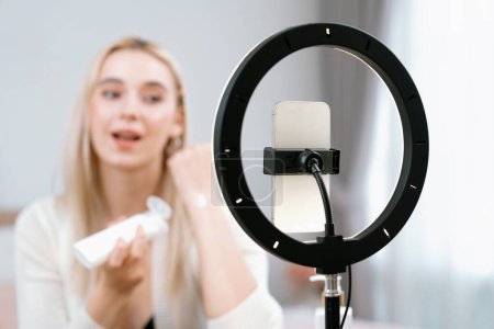 Photo for Young woman making beauty and cosmetic tutorial video content for social media. Beauty blogger smiles to camera while showing how to apply beauty skincare to audience or followers. Blithe - Royalty Free Image