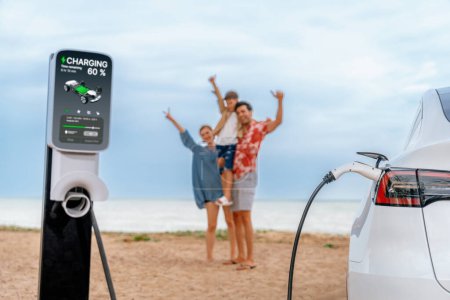 Photo for Alternative family vacation trip traveling by the beach with electric car recharging battery from EV charging station with blurred cheerful and happy family enjoying the seascape background. Perpetual - Royalty Free Image