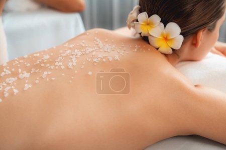 Closeup woman customer having exfoliation treatment in luxury spa salon with warmth candle light ambient. Salt scrub beauty treatment in health spa body scrub. Quiescent