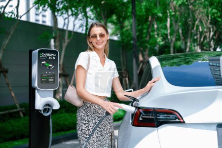 Les jeunes femmes voyagent avec la voiture électrique EV charge dans le jardin vert durable de la ville en plein air en été. Style de vie urbain durable par vert propre énergie rechargeable des véhicules électriques BEV à l'intérieur