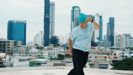 Photo for Caucasian B-boy dancer practicing street dancing at rooftop with city or urban. Motion shot of young man performing street dance by doing freeze pose. Break dance. Outdoor sport 2024. Endeavor. - Royalty Free Image