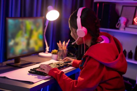 Host channel of young beautiful Asian gaming streamer playing fighting Moba at battle arena game on pc screen with multiplays, wearing pastel headphone at neon digital light modern room. Stratagem.