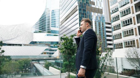 Photo for Skilled businessman talking to marketing team about marketing strategy by using phone while standing at skyscraper. Happy manager calling colleague about increasing sales at modern urban city. Urbane. - Royalty Free Image