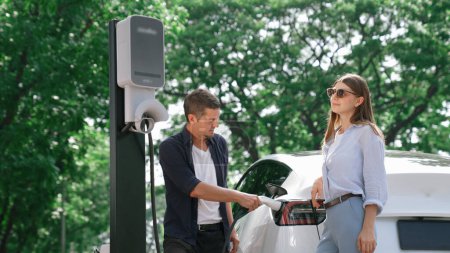 Elektroautos laden Strom für die Batterie von Liebespaaren, die während ihrer Autoreise mit umweltfreundlichen Elektrofahrzeugen im Nationalpark und im grünen Wald unterwegs sind. Erhöhen