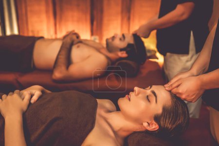 Téléchargez les photos : Couple client appréciant relaxant anti-stress massage de la tête et choyer beauté faciale loisirs de la peau dans la bougie chaude éclairage spa salon d'ambiance dans un complexe de luxe ou un hôtel. Tranquillité - en image libre de droit