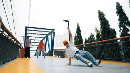 Photo for Panorama shot of professional hipster perform b-boy performance and energetic footstep. Skilled happy man practice break dance while friend cheering him at bridge. Outdoor sport 2024. Sprightly. - Royalty Free Image