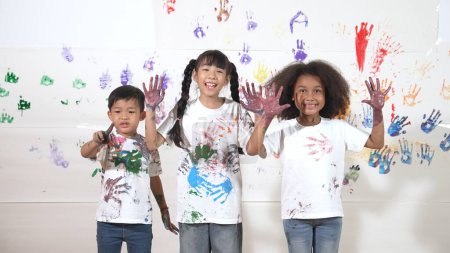 Photo for Diverse students put hands up together show colorful stained hands. Group of multicultural learner standing at white background with stained hands while looking at camera in lively mood. Erudition. - Royalty Free Image