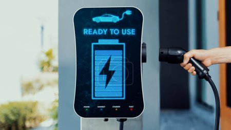 Photo for Home electric charging station showing battery status interface on screen with hand holding EV charger. Technological advancement of alternative energy sustainability and EV car. Peruse - Royalty Free Image