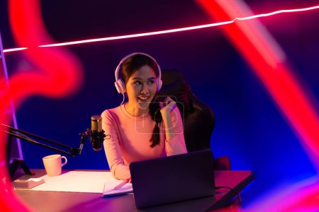 Photo for Smiling creative young beautiful Asian influencer talking in positive podcast speech in red frame at night time, using laptop for presentation online at pink neon light modern studio. Stratagem. - Royalty Free Image