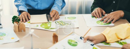 Photo for Green business meeting represented renewable energy. Skilled businesspeople discuss green business investment at table with environmental documents. Closeup. Focus on hand. Delineation. - Royalty Free Image