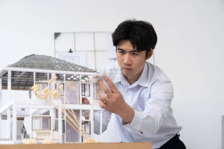 Téléchargez les photos : Portrait de l'ingénieur architecte professionnel asiatique se concentrer sur l'utilisation règle pour mesurer la longueur du modèle de maison tout en analysant la structure de la maison. Maison d'affaires créative et concept de design. Immaculée. - en image libre de droit