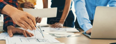 Photo for Architect team discuss about blueprint design at modern meeting room while her coworker working on laptop on table with blueprint and architectural equipment scattered around. Closeup. Delineation. - Royalty Free Image