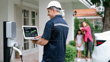 Photo for Qualified technician work on home EV charging station installation, make troubleshooting and configuration setup on charging system with laptop for EV at home with family present. Panorama Synchronos - Royalty Free Image