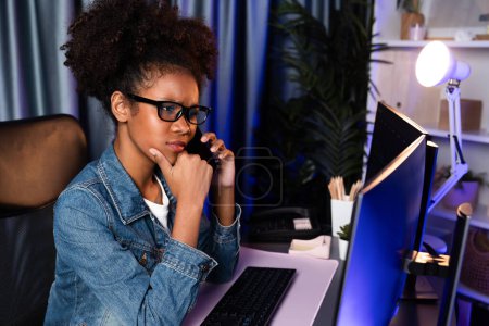 Foto de Mujer africana joven asombrada mirando en la computadora portátil del monitor de pantalla, llamando con un amigo en el teléfono inteligente, usando una camisa vaquera. Pensar en la planificación del proyecto de trabajo o estudiar nuevas tecnologías en el lugar de trabajo. Tastemaker. - Imagen libre de derechos