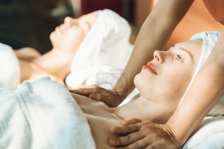 A portrait of two beautiful woman having back massage by professional masseur and falling in deep relaxation surrounded by traditional spa environment. Calming and relaxing concept. Tranquility.
