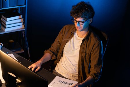 Photo for Young businessman reading design thinking on paper for new project surround work desk at neon light modern office. Thinking new next job sketching on notebook before sending present via email. Gusher. - Royalty Free Image