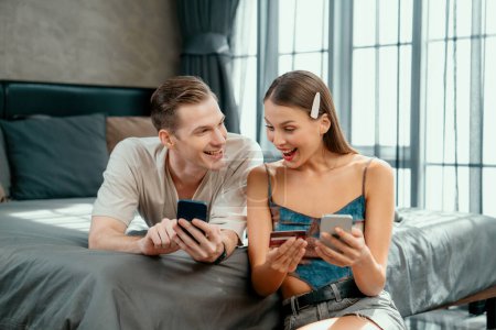 Photo for Young couple sit in the home bedroom using online payment app and digital wallet on smartphone to pay with credit card. E commerce shopping and modern purchasing via mobile internet. Unveiling - Royalty Free Image