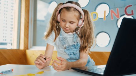 Photo for Pretty girl wearing headphone while study electronic equipment. Caucasian child doing science experiment while laptop, screwdriver and wires placed near on table. Smart online classroom. Erudition. - Royalty Free Image