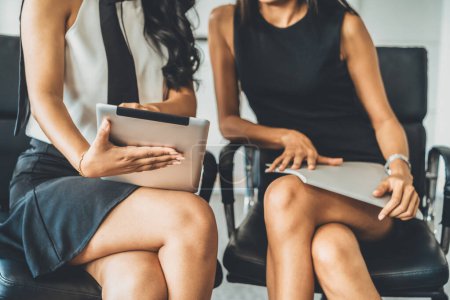 Photo for Two businesswomen discussing business while looking at financial data in their hands. They are sitting on the chairs in the office meeting room. uds - Royalty Free Image