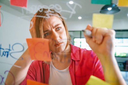 Photo for Closeup of young beautiful caucasian business leader presents marketing idea while writing marketing idea on glass board with mind map and colorful sticky notes. Portrait. Brainstorm. Immaculate. - Royalty Free Image
