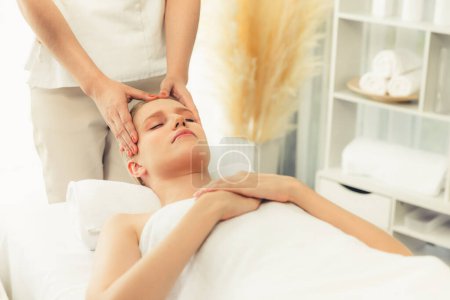 Téléchargez les photos : Femme caucasienne profiter relaxant anti-stress massage de la tête et choyer beauté du visage loisirs de la peau dans dayspa lumière moderne ambiant au complexe de luxe ou un salon de spa de l'hôtel. Tranquillité - en image libre de droit