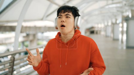 Dancer listen to hip hop music while sing along and walking at corridor. Handsome hipster wearing stylish cloth and headphone express feeling of lively or happy mood. Outdoor sport 2024. Sprightly.