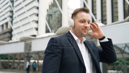 Foto de Hombre de negocios feliz usando auriculares escuchando música relajante y moverse a lo largo de la música mientras camina por la calle en la ciudad urbana con humor animado. Gerente de usar auriculares y disfrutar de escuchar rima relajante. Urbane. - Imagen libre de derechos