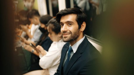 Photo for Smiling caucasian business man looking at mobile phone or playing social media while sitting in train. Attractive project manager going to work place by using public transport in rush hour. Exultant. - Royalty Free Image
