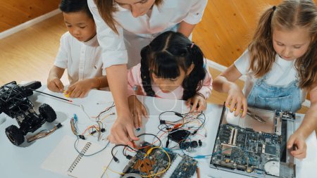 Photo for Top view of caucasian teacher teaching diverse students about electronic board. Multicultural children learn about digital electrical tool and fixing motherboard by using chips and wires. Erudition. - Royalty Free Image