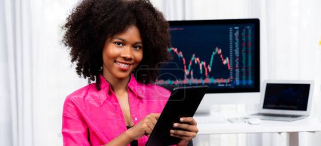 Téléchargez les photos : Analytique jeune femme d'affaires afro-américaine, spécialiste du trading boursier réussi, contre graphique de données dynamiques affichant l'analyse des tendances marketing à l'écran. Tastemaker. - en image libre de droit