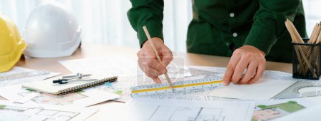 Photo for Professional engineer measuring the blueprint. Professional engineer working architectural project at studio on a table with yellow helmet and architectural equipment scatter around. Delineation. - Royalty Free Image