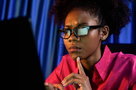 Téléchargez les photos : La blogueuse africaine qui travaillait s'est concentrée sur l'écran d'ordinateur portable avec un visage sérieux, cherchant l'analyse des données marketing, concluant le document global sur la base de données pour le rapport de réunion. Tastemaker. - en image libre de droit