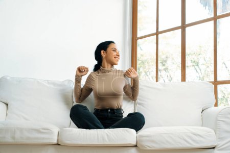Téléchargez les photos : Jeune femme afro-américaine étirant les bras pour une relaxation cruciale à la maison. La femme heureuse passe le week-end matin dans le salon. - en image libre de droit