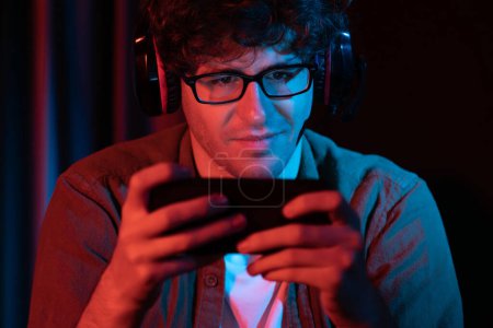 Photo for Smiling young gaming streamer team playing with Esport online on smartphone fighting wearing headphones at neon light room. Practising strategy plan to win competitors for next harder level. Gusher. - Royalty Free Image