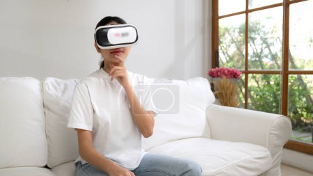Téléchargez les photos : Jeune femme utilisant réalité virtuelle VR masque à la maison pour vivre l'expérience d'achat en ligne. L'innovation VR en réalité virtuelle optimisée pour le divertissement numérique féminin. - en image libre de droit