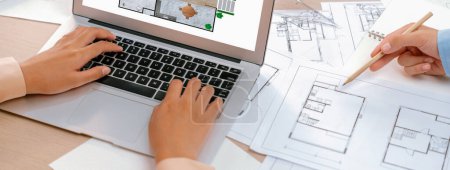 Photo for Eco house blueprint displayed on a laptop. Professional architect hand draws blueprint on meeting table with architectural document scatter around. Focus on hand. Closeup. Delineation. - Royalty Free Image