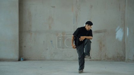 Photo for Handsome hipster practicing break dancing while listening music from headphone with cement background. Motion shot of street dancer perform robot dance. Outdoor sport 2024. Modern dance. Endeavor. - Royalty Free Image