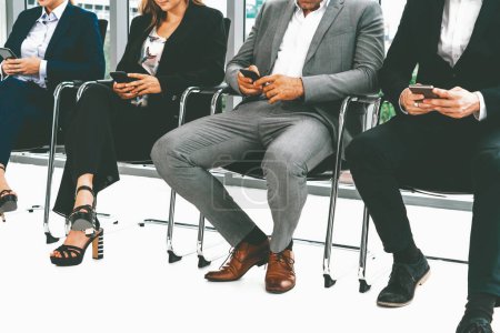 Téléchargez les photos : Femmes d'affaires et hommes d'affaires utilisant le téléphone portable tout en attendant sur les chaises dans le bureau pour l'entrevue d'emploi. Concept d'entreprise et de ressources humaines. uds - en image libre de droit