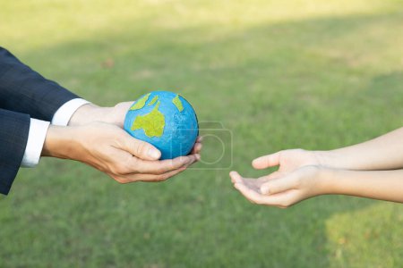 Téléchargez les photos : Businessman main donnant globe terrestre à petit garçon que le concept du Jour de la Terre en tant que responsabilité sociale d'entreprise pour contribuer à une protection de l'environnement plus verte pour la génération future durable. Pneumatique - en image libre de droit