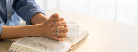 Photo for Asian male folded hand prayed on holy bible book while holding up a pendant crucifix. Spiritual, religion, faith, worship, christian and blessing of god concept. Blurring background. Burgeoning. - Royalty Free Image