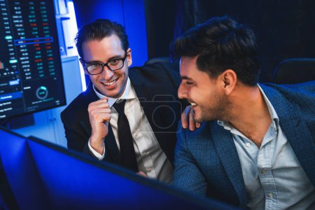 Photo for Two stock exchange traders discussing on dynamic successful investment graph, pointing trending of high profit in currency stock in financial data on monitor in neon light at workplace. Sellable. - Royalty Free Image