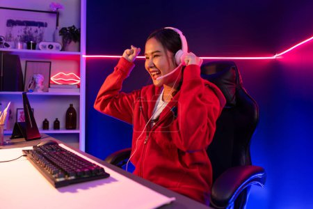 Photo for Host channel of smiling beautiful Asian girl streamer playing with raising fist up winning on Esport skilled team players wearing headphones pastel color, fighting online game at neon room. Stratagem. - Royalty Free Image