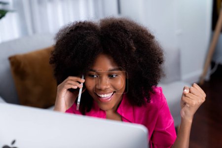 Foto de Mujer africana hablando con su compañero de trabajo o amigo por teléfono y mirando a la pantalla con la cara feliz. Logro para promover el puesto de trabajo en la empresa con la vida de las buenas noticias. Tastemaker. - Imagen libre de derechos