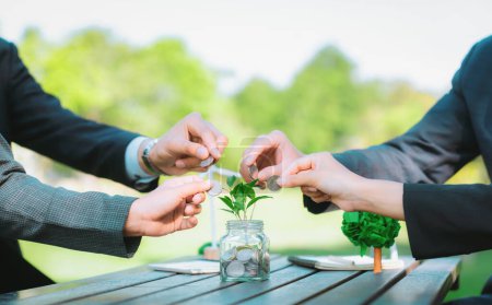 Geschäftsleute legen Münzen in Spargläser als nachhaltige Geldanlage oder Öko-Subvention auf den Tisch. Grüne Unternehmen fördern und investieren das Umweltbewusstsein. Kreisel